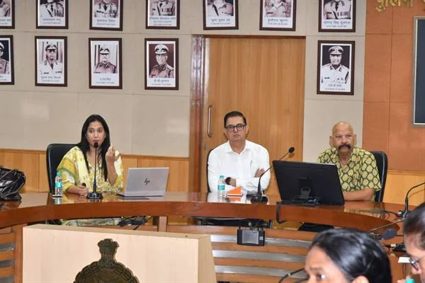 सभागार में मंच पर अधिकारियों का पैनल और प्रोजेक्टर स्क्रीन, सामने पंक्तियों में श्रोता